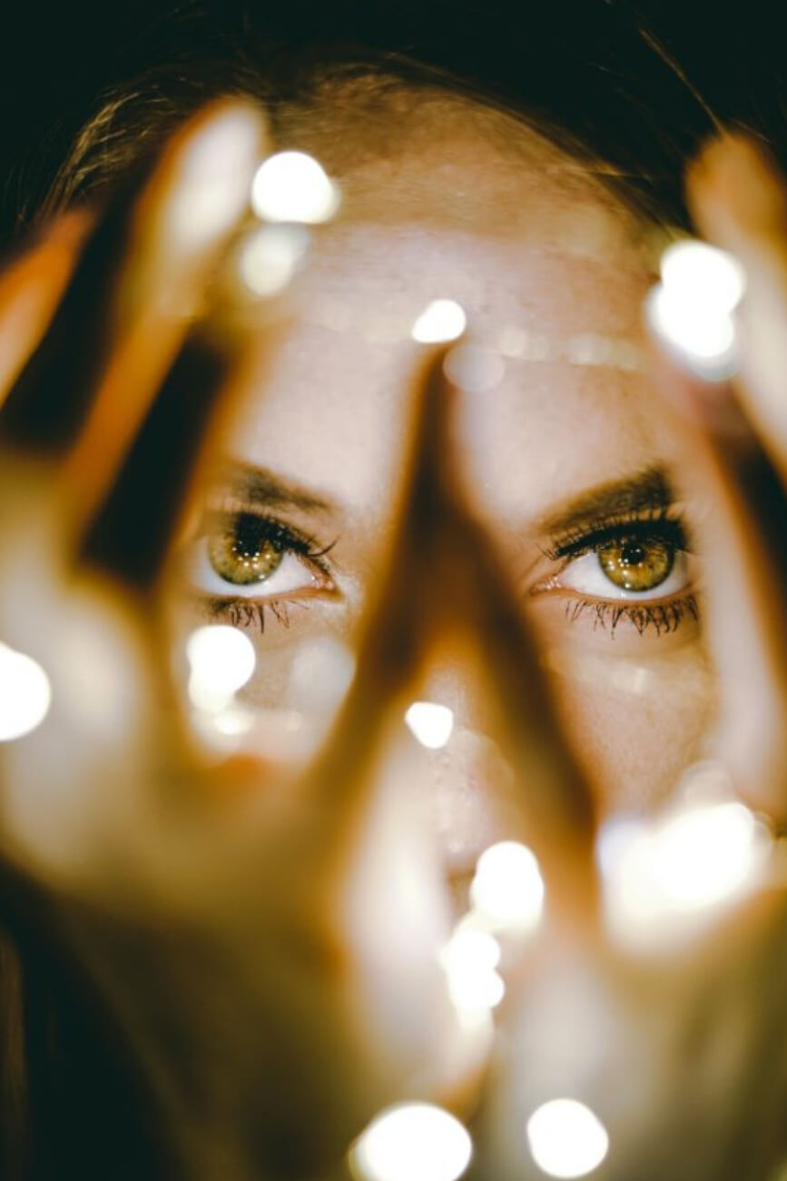 KL Tarot. Person's eyes peering through a cluster of blurred lights held in front, creating a glowing effect.